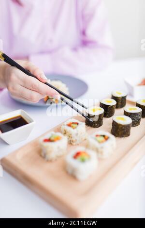 Close up of female eating sushi portion roll with chopsticks at restaurant. Stock Photo
