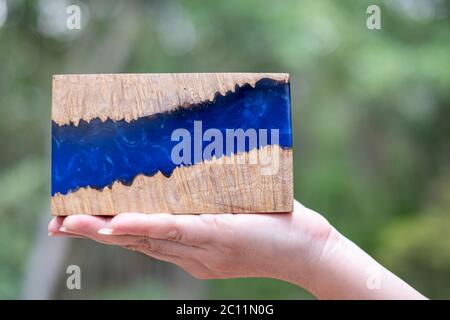 Hand holding cube casting epoxy resin with nature burl maple wood on green blurred background Stock Photo