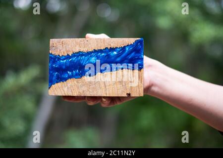 Hand holding cube casting epoxy resin with nature burl maple wood on green blurred background Stock Photo