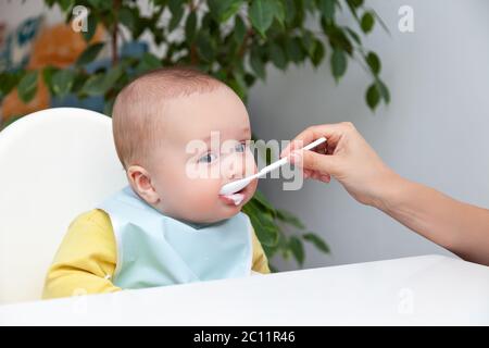 First feeding of baby boy, eat yoghurt, dirty mouth, holds spoon Stock Photo