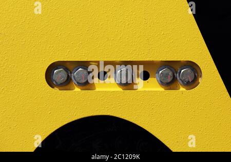 cap screws and holes in the yellow-black background - on the construction equipment compactor. Stock Photo