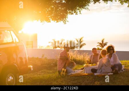 Picnic and outdoor leisure activity for group of adult and young people enjoy friendship together - travel and fun concept with. freinds and sunset - Stock Photo
