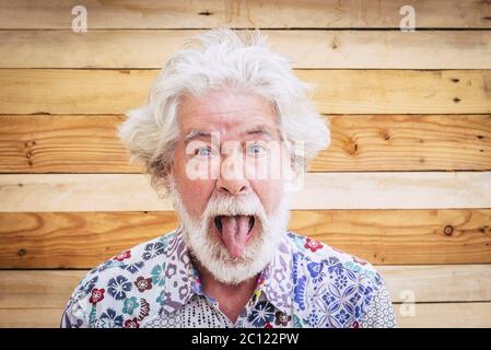 Portrait of cheerful caucasian senior crazy man with wood background - alternative and young old male in funny expression -white hair and beard for di Stock Photo