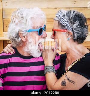 Portrait of cheerful caucasian senior crazy couple with wood background - alternative and young old people in funny expression -white hair and beard a Stock Photo