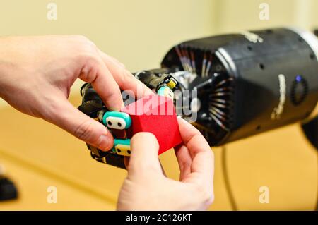 Man Lets Robot Hand Holding a Red Cube in Research Laboratory. Stock Photo