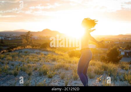 Attractive young woman spinning with open arms at mountain top against sunset. Cute hot girl improvises and enjoy fredoom in nature while smiling and Stock Photo