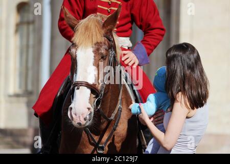 woman and child stroking a red horse on which the rider sits, dressed in period costume Stock Photo