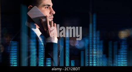 Young Caucasian entrepreneur talking on smartphone on dark background, collage with finance nimbers and graphs Stock Photo
