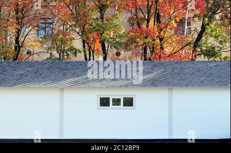 White wall texture house, dark box, flexible brown tiles on the background of multi-colored leaves autumn forest. Stock Photo