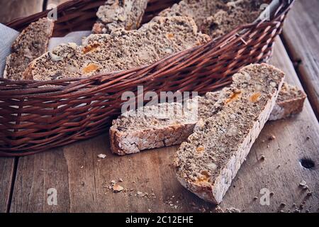 slices of rustic brown bread with nut and apricot pieces and a wicker basket on a kitchen table Stock Photo