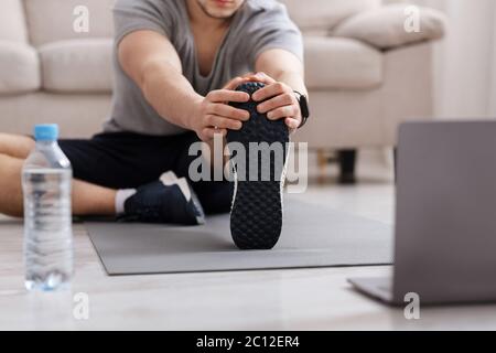 Gym at home. Man doing stretching on floor at home, water and laptop near Stock Photo