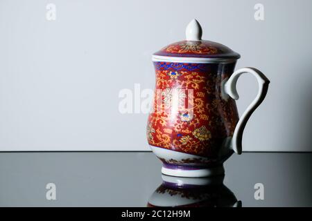 A red teapot with design on it placed on a reflective table in a white background Stock Photo