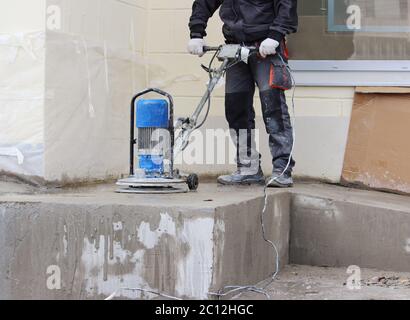 male worker works with the diamond grinding machine, polishing the porch in front of the office building. the cement floor  and Stock Photo