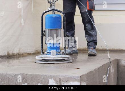 male worker works with the diamond grinding machine, polishing the porch in front of the office building. the cement floor  and Stock Photo
