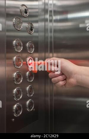 Young man using a contactless tool to press an elevator button, to avoid the spread of the coronavirus disease, Covid-19. New normal. Stock Photo