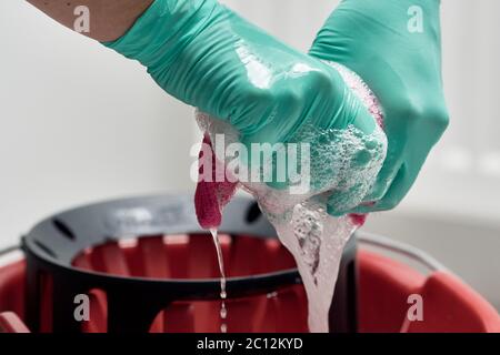 Close-up of hands with gloves wringing out cleaning cloth over bucket filled with water and soap Stock Photo