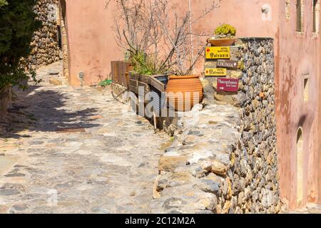 Monemvasia, Greece - March 31, 2019: Street view with old houses and hotel direction arrows in ancient town, Peloponnese Stock Photo