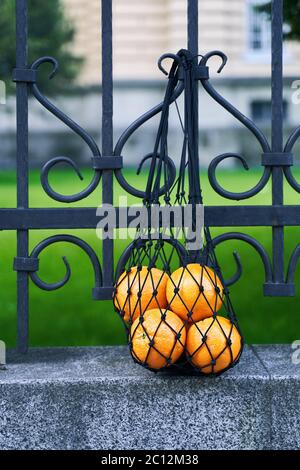 Black mesh bag full of oranges as a symbol of zero waste lifestyle is hanging on the wrought iron fence Stock Photo