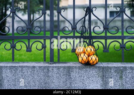 Black mesh bag full of oranges as a symbol of zero waste lifestyle is hanging on the wrought iron fence Stock Photo