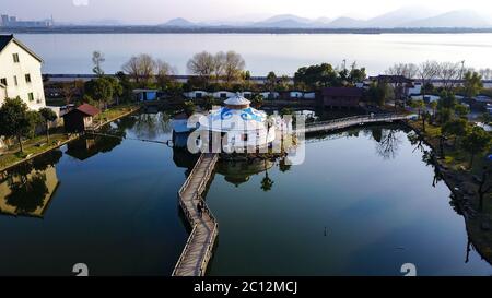 Aerial view on Mongolian white styled Yurt with blue ornaments in the middle of a small water reservoir with two bridges. Stock Photo