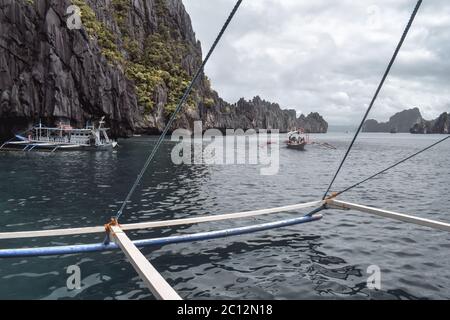 Tourists on traditional Philippino fisherman boats crossing the waters near grey limestone cliffs of El Nido at Palawan Island the Philippines Stock Photo