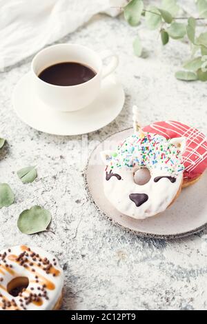 Cakes donuts with a cup of espresso over light background. Table with morning breakfast dessert and coffee. Trendy doughnut unicorn with white glaze. Stock Photo