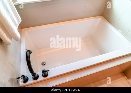 Rectangular bathtub with black faucet and handles against tile wall and floor Stock Photo