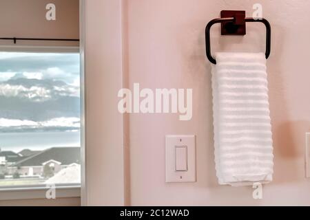 White towel hanging on square towel holder beside electrical rocker light switch Stock Photo
