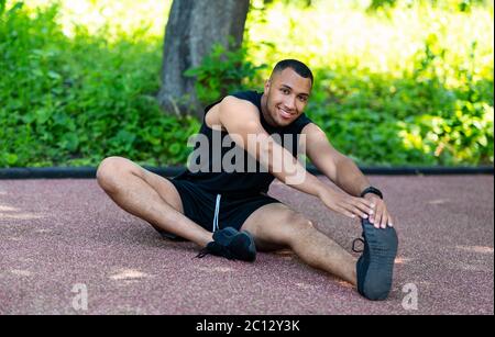 Handsome African American athlete stretching on jogging track in park Stock Photo