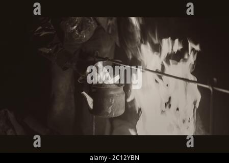 Hand of man taking the kettle, wich heated on a bright fire at night outdoor, black and white photo Stock Photo