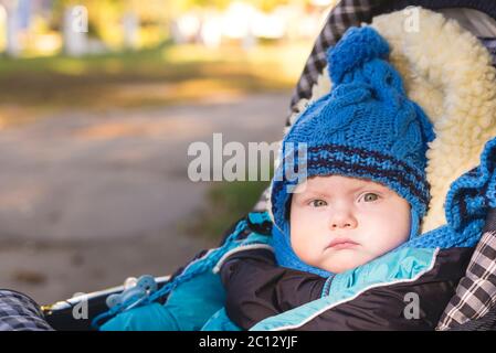 A small child in a hat and scarf sitting in a stroller in autumn Stock Photo