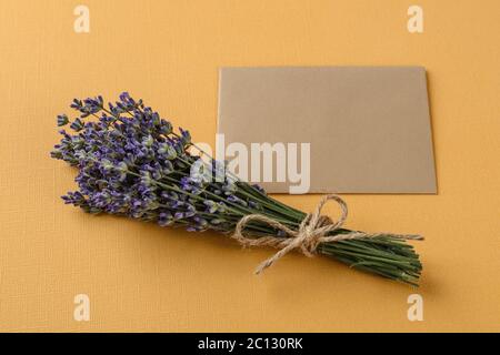 Bouquet of fragrant blooming lavender near a blank of brown paper for notes over a textural yellow background. Summer and romantic greeting card. Stock Photo