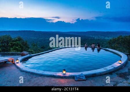 Three people relax at dusk in the swimming pool overlooking Lake Mburo National Park at Mihingo Lodge, Uganda Stock Photo