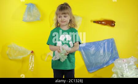 Girl activist volunteer in t-shirt with recycle logo. Collects cellophane packages from ground. Background with bags, bottles. Save earth environment. Plastic trash nature pollution Stock Photo