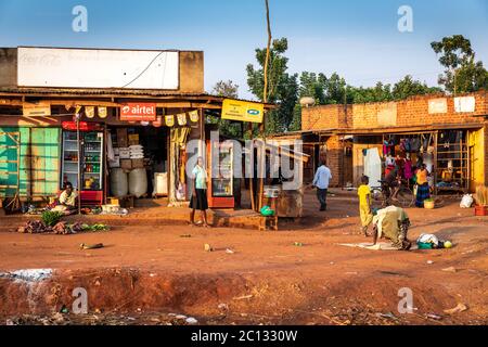 Roadside shops in rural Ugandan village with children in the street and a red dirt road, Uganda, Africa Stock Photo