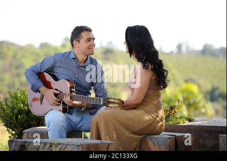 portrait of beautiful young wedding couple posing in outdoor photoshoot playing guitar Stock Photo