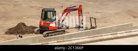 Orange excavator parked next to a concrete platform. Construction site. Aerial angled view. Stock Photo