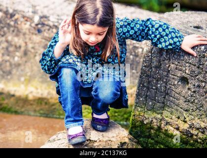 pretty little girl playing on a rock at the water's edge Stock Photo