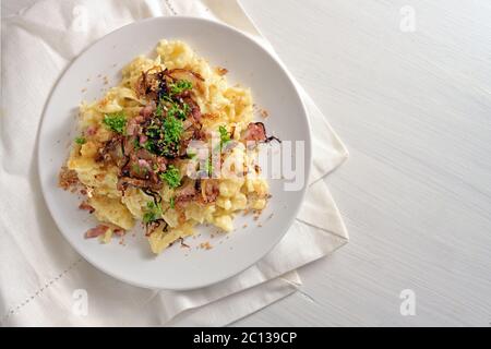 Spaetzle, homemade egg noodles with cheese, roasted bacon, onion and breadcrumbs, served with parsley garnish on a white painted wooden table, traditi Stock Photo