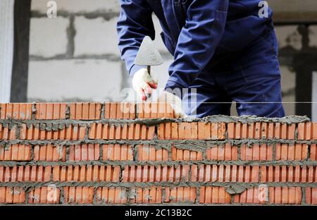 professional construction worker laying bricks and building house on industrial site Stock Photo