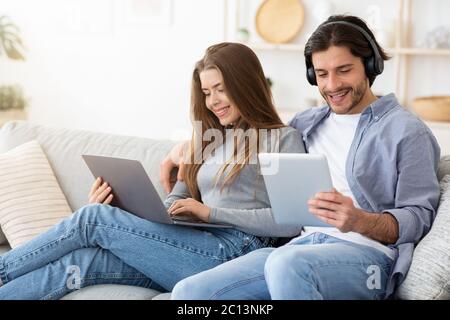 Smiling man and woman using electronic devices, home interior Stock Photo