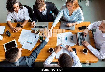 Business Partners Shaking Hands Sitting At Table In Office, Above-View Stock Photo