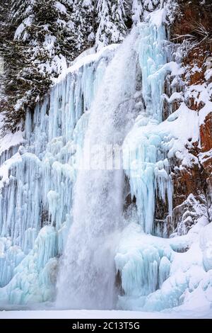 Tall cascading ice cold river water raging over icy rocks Stock Photo