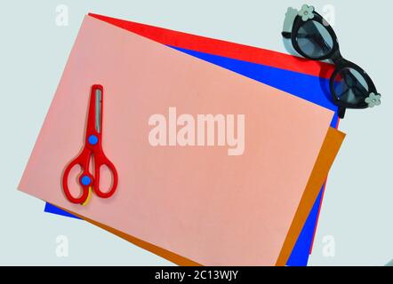 colour papers, scissors and specs on a white surface indicating a kid's activity desk Stock Photo