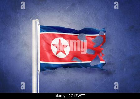 Torn flag of North Korea flying against grunge background Stock Photo