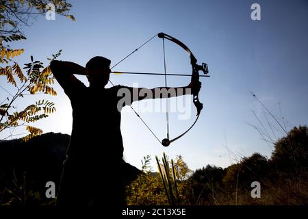 Archer draws his compound bow silhouette Stock Photo