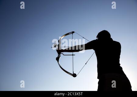 Archer draws his compound bow silhouette Stock Photo