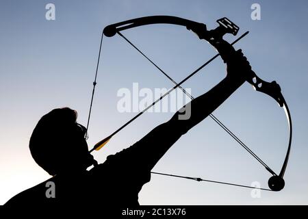 Archer draws his compound bow silhouette Stock Photo