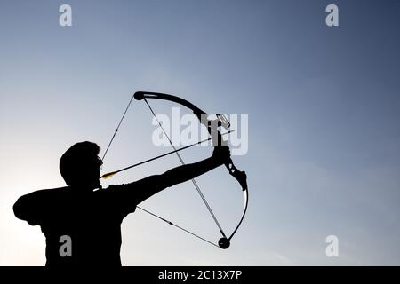 Archer draws his compound bow silhouette Stock Photo