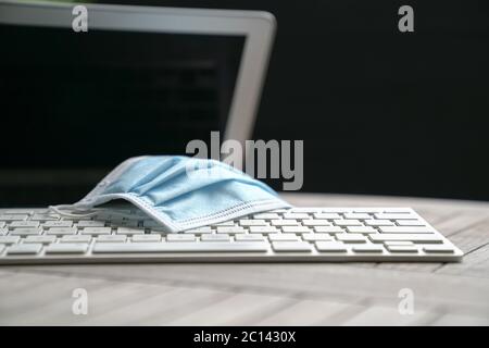Medical face mask on top of computer laptop. Work at home during covid-19 concept. Stock Photo